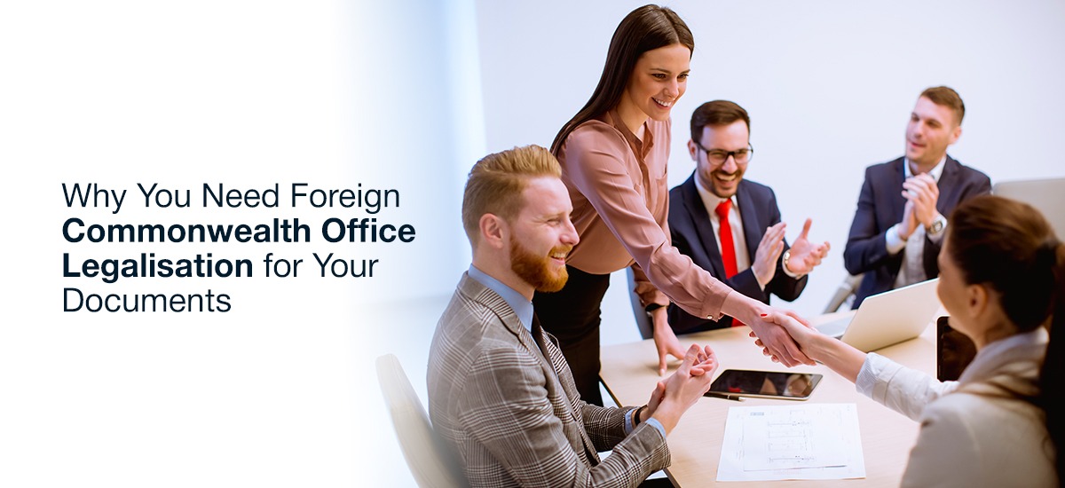 Professional business meeting with colleagues celebrating a successful agreement, featuring a confident woman in a pink blouse shaking hands with a client, highlighting the importance of Foreign Commonwealth Office Legalisation for documents.